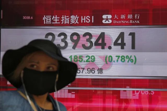 A woman wearing a face mask walks past an electronic board showing Hong Kong share index outside a local bank in Hong Kong, Tuesday, April 7, 2020. Asian shares are rising, echoing the rally on Wall Street fueled by signs of hope that the coronavirus pandemic could be slowing. (Photo by Kin Cheung/AP Photo)