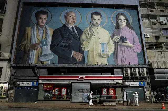 City workers disinfect a bus stop to help prevent the spread of new coronavirus outside a closed cinema featuring a mural of film directors, from left, Federico Fellini, Alfred Hitchcock, Luis Buñuel and Lucrecia Martel in Montevideo, Uruguay, just after midnight on Monday, April 20, 2020. (Photo by Matilde Campodonico/AP Photo)