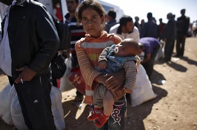 Rula, an eight-year-old Syrian Kurdish refugee girl holding her three-month-old brother Ciwan, waits for transportation after crossing into Turkey near the southeastern Turkish town of Suruc in Sanliurfa province October 1, 2014. (Photo by Murad Sezer/Reuters)