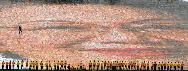 College students line a grass verge next to a giant photo mosaic of former late Philippine president and democracy icon Corazon Aquino at the Quirino Grandstand in Manila. President Benigno Aquino led the unfurling of the photo mosaic, which is composed of 3,200 photos and weighs almost 4 tons, to honor his mother, Corazon Aquino, on the first anniversary of her death. The photo mosaic, measuring 250 feet by 200 feet, was made in an attempt to earn entry into the Guinness World Records book. (Photo by Noel Celis/AFP/Getty Images)