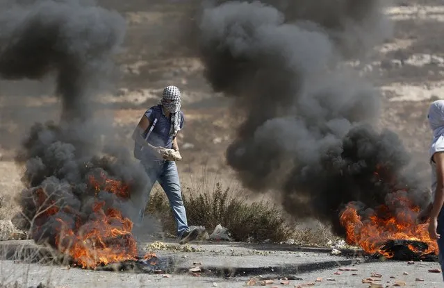 A Palestinian protester holds a rock as he walks past burning tyres during clashes with Israeli troops near the Jewish settlement of Bet El, near the occupied West Bank city of Ramallah October 5, 2015. (Photo by Mohamad Torokman/Reuters)