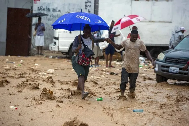 A woman is helped by a man to cross a flooded street during the passing of Tropical Storm Laura in Port-au-Prince, Haiti, Sunday, August 23, 2020. (Photo by Dieu Nalio Chery/AP Photo)