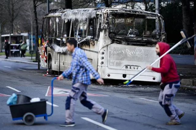 Two men cross the street in front of a burned-out bus standing beneath a residential building, in the district Neukoelln in Berlin, Germany, Tuesday, January 3, 2023. People across Germany on Saturday resumed their tradition of setting off large numbers of fireworks in public places to see in the new year. The bus was set on fire during the New Year's celebrations. (Photo by Markus Schreiber/AP Photo)