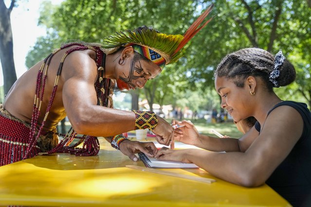 Txatxu Pataxo, left, of the Pataxo people of Bahia, Brazil, shows Eva Quiroz, 16, of Takoma Park, Md., how to draw a pattern traditional used in body painting, during the opening day of the Smithsonian Folklife Festival, Wednesday, June 26, 2024, on the National Mall in Washington. This year's festival theme is “Indigenous Voices of the Americas” and will run through July 1. “There was really no language barrier”, says Quiroz, “because it's art and that's universal”. (Photo by Jacquelyn Martin/AP Photo)