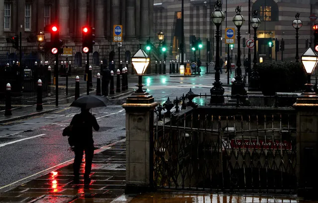 A man with an umbrella walks through a street in the financial area of London, Wednesday, January 13, 2021 during England's third national lockdown to curb the spread of coronavirus. (Photo by Alastair Grant/AP Photo)