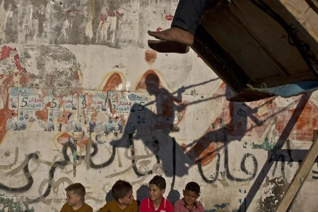In this Monday, July 20, 2015, file photo, the shadow of Palestinian refugee boys is cast on a wall while enjoying a ride on an improvised swing during Eid al-Fitr holiday at Baqaa Refugee Camp in Amman, Jordan. (Photo by Muhammed Muheisen/AP Photo)