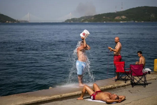 People cool off at the Bosphorus as a forest fire smoke rises, background, during a hot summer day in Istanbul, Turkey, Wednesday, July 26, 2023. Water-dropping planes, helicopters and firefighters were also deployed to fight a blaze that broke out Wednesday at a forest near the district of Beykoz, in Istanbul, where temperatures reached 43 C. (Photo by Francisco Seco/AP Photo)