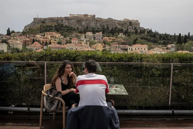 A man and a woman drink coffee in the Monastiraki district of Athens,with the ancient Acropolis hill in the background, Monday, May 3, 2021. Cafes and restaurants have reopened in Greece for sit-down service for the first time in nearly six months, as the country began easing coronavirus-related restrictions with a view to opening to the vital tourism industry in the summer. (Photo by Petros Giannakouris/AP Photo)