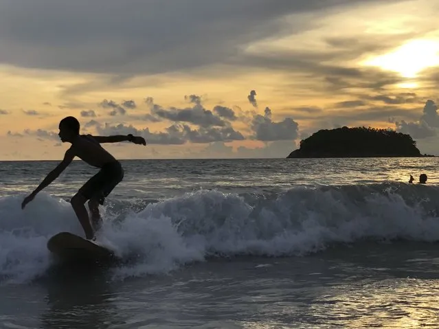 A surfer catches a wave as the sun sets over Kata Beach on the resort island of Phuket, Thailand on Sunday, May 26, 2019. Thailand hopes to first fully reopen the island of Phuket, its most popular destination, by July 1 for vaccinated visitors without quarantine. But they will be required to spend a certain time, possibly up to a week, on Phuket before they are allowed to travel elsewhere in Thailand. (Photo by Adam Schreck/AP Photo)