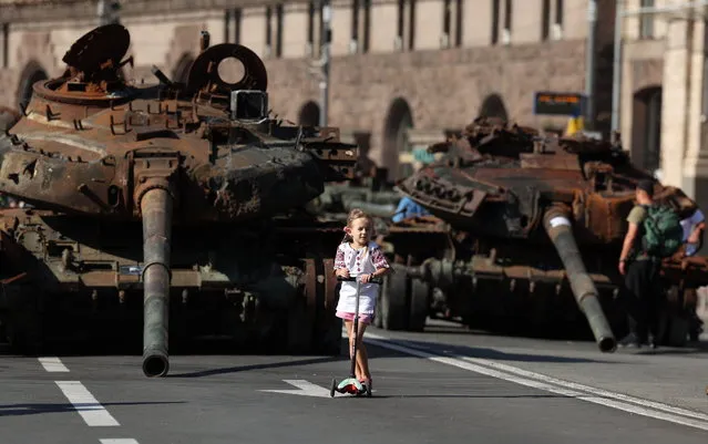 A girl rides her scooter past damaged Russian armored military vehicles that were seized by the Ukrainian army amid the Russian invasion, along Khreshchatyk Street in Kyiv, Ukraine, 24 August 2023. The damaged Russian military machinery has been set up in downtown Kyiv to form part of the Independence Day celebrations, which take place on 24 August. (Photo by Cathal McNaughton/EPA)