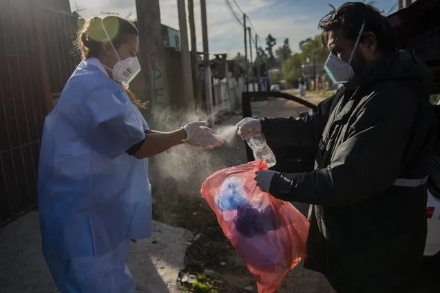 Driver Jose Maria Ruiz disinfects doctor Carolina Moreira after a home visit of a COVID-19 patient in Montevideo, Uruguay, Monday, May 31, 2021. (Photo by Matilde Campodonico/AP Photo)