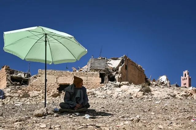 A resident sits in the shade of an umbrella near a mosque and buildings damaged by the September 8 earthquake in the village of Moulay Brahim in al-Haouz province in the High Atlas mountains of central Morocco on September 11, 2023. The 6.8-magnitude quake struck the Atlas mountains southwest of the tourist centre of Marrakesh. It killed almost 2,500 people and injured a similar number, according to the latest official toll issued on September 11. (Photo by Philippe Lopez/AFP Photo)