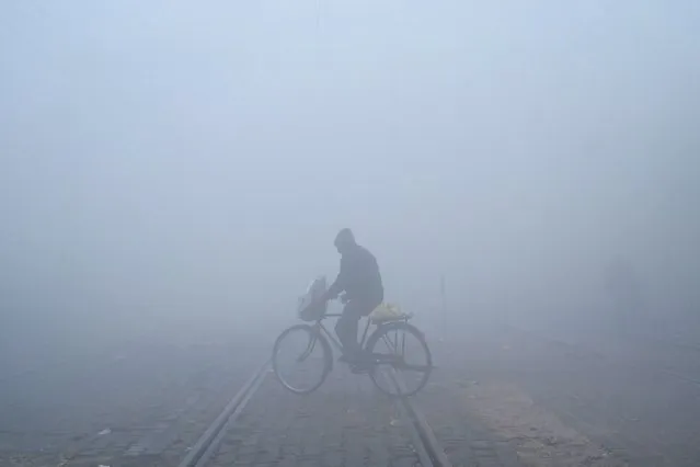 A cyclist crosses a railway track amid dense fog on a cold winter morning in Amritsar on December 26, 2023. (Photo by Narinder Nanu/AFP Photo)