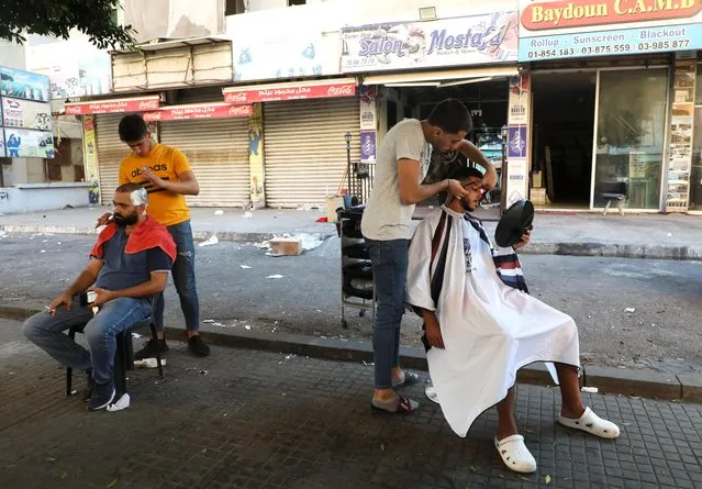 Barbers shave their customers outside their shop due to a power cut in Beirut, Lebanon, August 20, 2021. (Photo by Mohamed Azakir/Reuters)