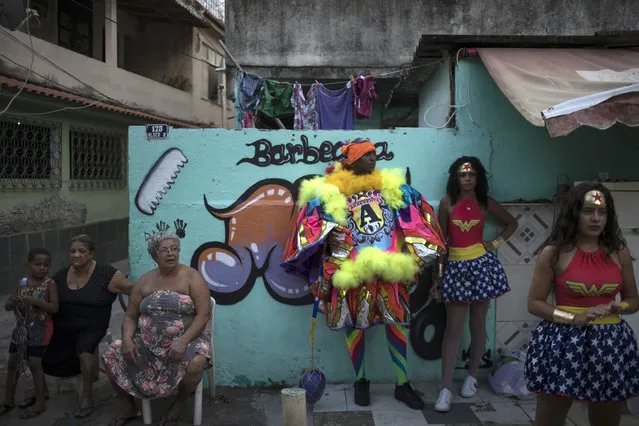 A “bate-bola”, center, stands next to residents and revelers wearing wonder woman costumes during carnival festivities at the Cidade de Deus, or “City of God” slum in Rio de Janeiro, Brazil, Monday, February 27, 2017. “Bate-bola” groups celebrate Brazil's Carnival by dressing in colorful costumes inspired by clowns and using a stick to slam a ball onto the ground and make some noise. (Photo by Felipe Dana/AP Photo)