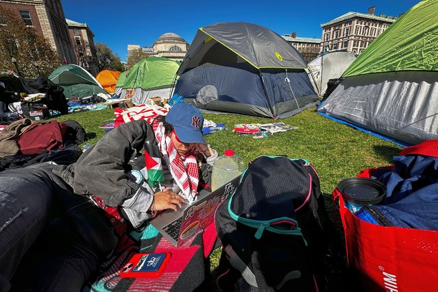 A pro-Palestinian demonstrator uses their computer at a protest encampment at the Columbia University campus, Monday, April 22, 2024, in New York. (Photo by John Minchillo/AP Photo)