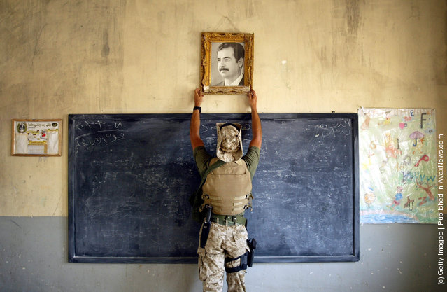A U.S. Marine pulls down a picture of Saddam Hussein