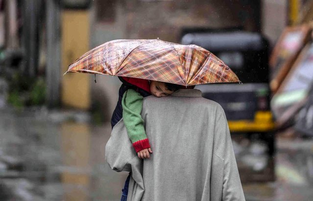 A man carries a child under an umbrella as it rains in Srinagar, Indian controlled Kashmir, Monday, April 29, 2024. (Photo by Mukhtar Khan/AP Photo)