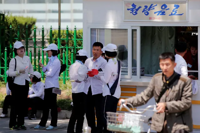 People, carrying props for an apparent parade to celebrate the Workers' Party of Korea (WPK) congress, eat ice-cream outside a snacks kiosk in central Pyongyang, North Korea May 8, 2016. (Photo by Damir Sagolj/Reuters)
