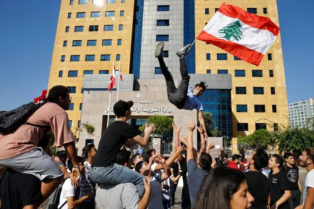 A student protester is thrown into the air by his colleagues as he holds a Lebanese flag during ongoing protests against the Lebanese government, in front of the education ministry in Beirut, Lebanon, Tuesday, November 12, 2019. (Photo by Bilal Hussein/AP Photo)