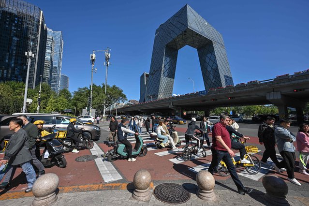 People cross a road in the business district in Beijing on October 8, 2024. (Photo by Adek Berry/AFP Photo)