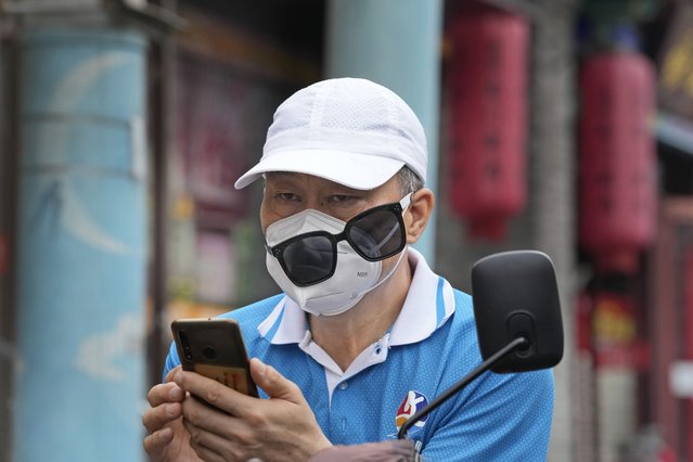A man wearing a mask lowers his sunglasses to look at his phone, Monday, June 27, 2022, in Beijing. (Photo by Ng Han Guan/AP Photo)