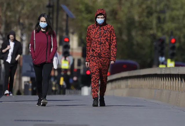 People wear protective face masks as they walk in Westminster in London, as the country is in lockdown to help curb the spread of coronavirus, Tuesday, April 21, 2020. (Photo by Kirsty Wigglesworth/AP Photo)