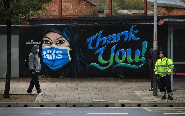 Two man are pictured in front of a piece of street art, created by The Artful Dodger, thanking the NHS on April 29, 2020 in London, England. British Prime Minister Boris Johnson, who returned to Downing Street this week after recovering from Covid-19, said the country needed to continue its lockdown measures to avoid a second spike in infections. (Photo by Andrew Redington/Getty Images)