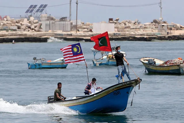 Palestinians ride a boat with flags during an event to show solidarity with countries affected by the coronavirus disease (COVID-19), at the seaport of Gaza City on May 18, 2020. (Photo by Mohammed Salem/Reuters)