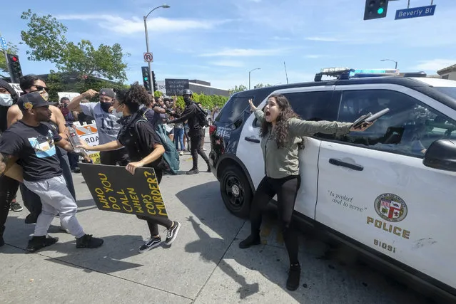 A person tries to stop others from attacking a police vehicle during a protest over the death of George Floyd in Los Angeles, Saturday, May 30, 2020. Protests across the country have escalated over the death of George Floyd who died after being restrained by Minneapolis police officers on Memorial Day, May 25. (Photo by Ringo H.W. Chiu/AP Photo)