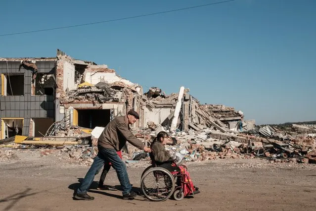 Disabled Rima Csikalenko (R), 65, is helped by neighbours to return to her home after receiving her monthly pension payment in the frontline town of Bakhmut in the Donetsk region on October 7, 2022, amid the Russian invasion of Ukraine. (Photo by Yasuyoshi Chiba/AFP Photo)