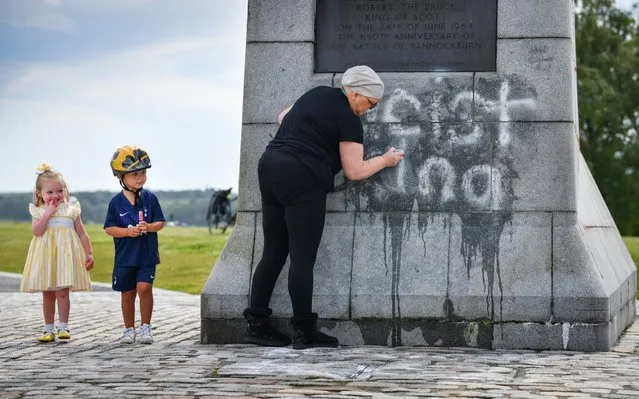 Children look on as a member of the public cleans the Robert the Bruce Statue which has been defaced with graffiti saying “Racist King” on June 12, 2020 in Bannockburn, Scotland. Following the removal of the Edward Colston statue during a Black Lives Matter protest in Bristol, a selection of statues across the UK have received increased scrutiny due to their links to racism and the slave trade. (Photo by Jeff J. Mitchell/Getty Images)
