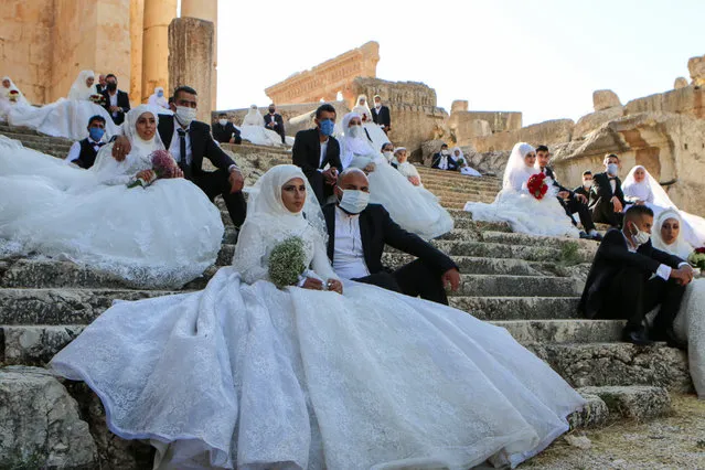 Lebanese couples, wearing protective face masks, sit on the steps during a group wedding at the Temple of Bacchus at the historic site of Baalbek in Lebanon's eastern Bekaa Valley on July 24, 2020, during the coronavirus pandemic. (Photo by AFP Photo/Stringer)