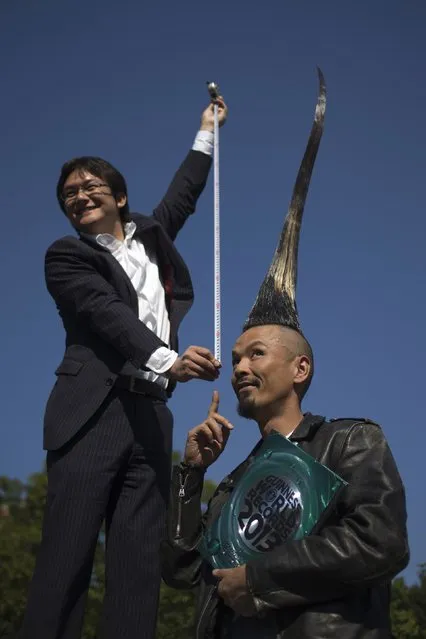 Television journalist Takashi Yanagisawa holds a measuring tape from atop a step ladder while interviewing Japanese fashion designer Kazuhiro Watanabe, who holds the world record for the “Tallest Mohawk”, during a media event held by the Guinness World Records to launch their 2013 book edition in New York September 12, 2012. According to the Guinness World Records, Watanabe's do stands at 3 feet 8.6 inches. (Photo by Adrees Latif/Reuters)