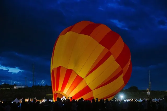 Attendees walk past a hot air balloon as it is lit by flame while being prepared for take off on the first day of the 2015 Albuquerque International Balloon Fiesta in Albuquerque, New Mexico, October 3, 2015. (Photo by Lucas Jackson/Reuters)