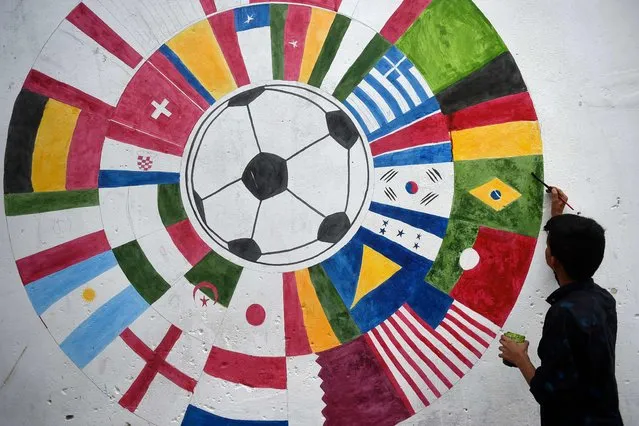 In this picture taken on November 7, 2022, a Pakistani soccer fan paints a wall mural of participating countries of the Qatar 2022 FIFA World Cup football tournament, along a street in Karachi. (Photo by Rizwan Tabassum/AFP Photo)