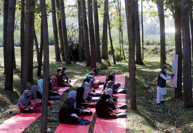 Students wearing protective face masks attend their class under the trees as they maintain social distancing outside their school, amid the coronavirus disease (COVID-19) outbreak, in Gund on the outskirts of Srinagar on September 30, 2020. (Photo by Danish Ismail/Reuters)