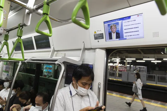 A train passenger plays a game on his cellphone under an onboard screen showing the news of U.S. President Donald Trump after he was tested positive for the coronavirus in Tokyo on Friday, October 2, 2020. (Photo by Hiro Komae/AP Photo)