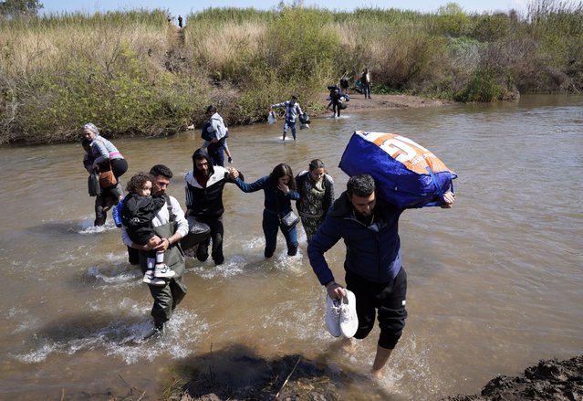 Syrian families who fled the clashes in Syria hold their luggages as they cross a river marking the border between Syria and northern Lebanon near the village of Heker al-Daher in Akkar province, Lebanon, Tuesday, March 11, 2025. (Photo by Hussein Malla/AP Photo)