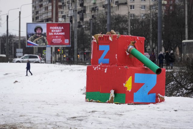 A man walks past a billboard with a portrait of a Russian soldier, a participant of the action in Ukraine and the words “The victory will be ours!” and a tank mockup made from boxes, in St. Petersburg, Russia, February 18, 2023. (Photo by Dmitri Lovetsky/AP Photo)