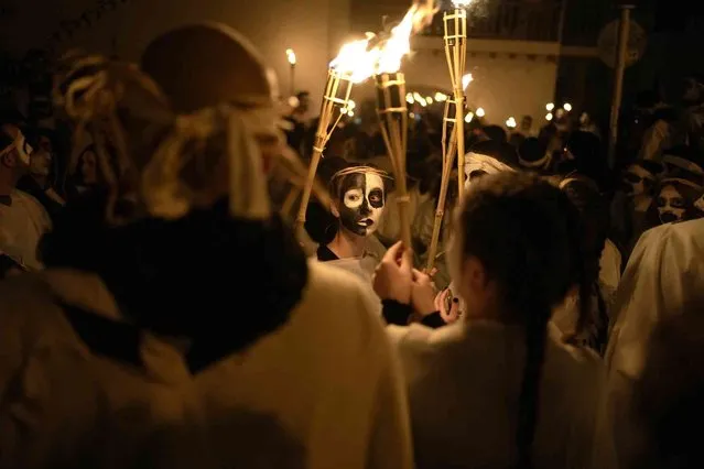 Young men and women with faces painted wear white sheets and hold torches on long poles, take part at the Torch Parade (Lampadiforia) on the Aegean Sea island of Naxos, Greece, late Saturday, February 25, 2023. The first proper celebration of the Carnival after four years of COVID restrictions, has attracted throngs of revellers, Greek and foreign, with the young especially showing up in large numbers. (Photo by Thanassis Stavrakis/AP Photo)