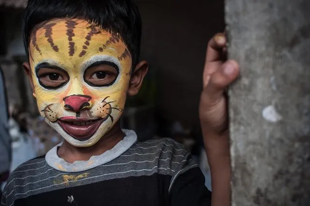 A boy with a painted tiger face poses before the Grebeg Ritual in Tegallalang, Bali, Indonesia, on May 1, 2013. During the biannual ritual young members of the community parade through the village with painted faces and bodies to ward off evil spirits. (Photo by Putu Sayoga/Getty Images)