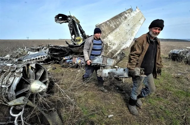 Local residents carry collected scrap metal near a destroyed military plane, amid Russia's invasion of Ukraine, in Kharkiv region, Ukraine on April 8, 2023. (Photo by Oleksandr Klymenko/Reuters)