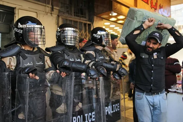 A man carrying a package walks past Iraqi riot police security forces standing guard outside the Central Bank of Iraq headquarters along Rashid Street in the centre of the capital Baghdad on December 22, 2020. Hundreds of angry Iraqis protest in several cities against a currency devaluation that has slashed their purchasing power amid a pandemic-fuelled economic crisis. The Central Bank of Iraq (CBI) at the weekend devalued the currency by over a fifth against the US dollar, officially re-pegging the dinar at a bank rate of 1,460 to the greenback. (Photo by Ahmad Al-Rubaye/AFP Photo)