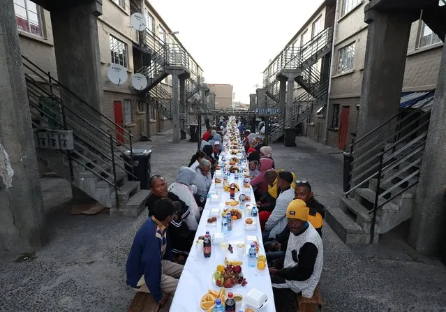 People sit at a long makeshift table before an Iftar, breaking of the fast, during the holy month of Ramadan in Heideveld on the Cape Flats, Cape Town, South Africa on April 15, 2023. (Photo by Esa Alexander/Reuters)