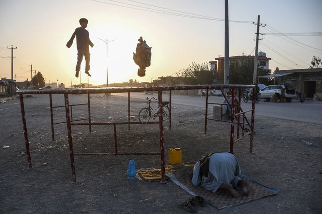 An Afghan man (bottom) offers prayers as children play on a trampoline along a road on the outskirts of Mazar-i-Sharif on September 9, 2025. (Photo by Atif Aryan/AFP Photo)