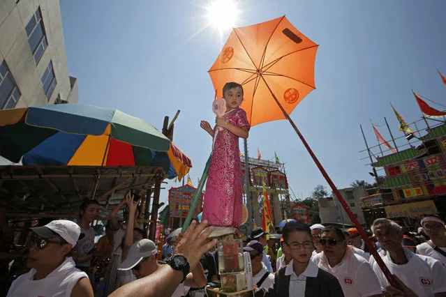 A child dressed in a traditional Chinese costume floats in the air, supported by a rig of hidden metal rods, during a parade on the outlying Cheung Chau island in Hong Kong to celebrate the Bun Festival Tuesday, May 22, 2018. Bun Festival, the Taoist God of the Sea, is worshipped and evil spirits are scared away by loud gongs and drums during the procession. The celebration includes bun scrambling, parades, opera performances, and children dressed in colorful costumes. (Photo by Kin Cheung/AP Photo)