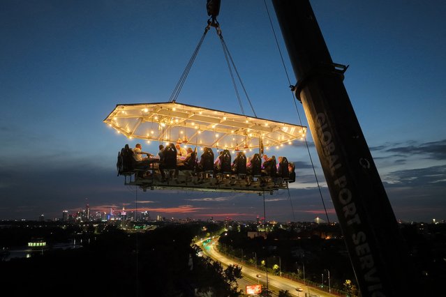This aerial view shows customers having dinner during an event organised by Belgian-based restaurant service “Dinner in the Sky”, which uses a crane to hoist its guests, table, and waiting staff 50 meters into the air, in Warsaw on August 17, 2024. (Photo by Sergei Gapon/AFP Photo)