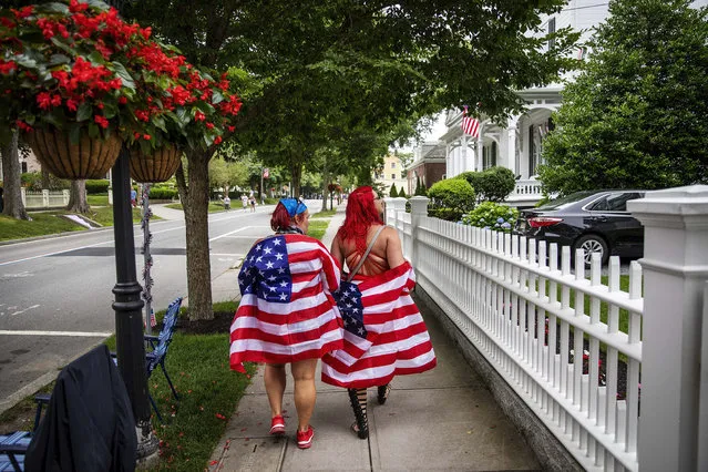 Parade goers draped in American flags walk down the street before a Fourth of July parade begins Saturday, July 4, 2020, in Bristol, R.I. The town, which lays claim to the nation's oldest Independence Day celebration in the country, held a vehicle-only scaled down version of its annual parade Saturday due to the coronavirus pandemic. (Photo by David Goldman/AP Photo)