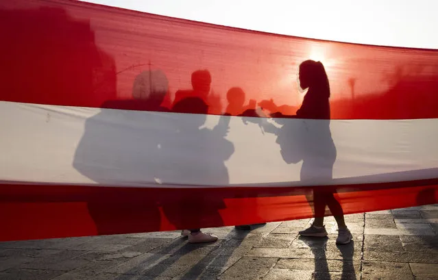Demonstrators are silhouetted on a Peruvian flag before a march to demand significant social changes and a new constitution from the government of new interim president Francisco Sagasti, in Lima, Peru, Wednesday, November 18, 2020. The march comes a day after the Peruvian Congress swore-in Sagasti, its third president in just over a week. (Photo by Rodrigo Abd/AP Photo)